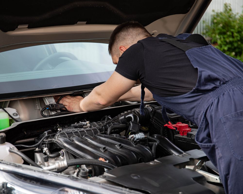 Mecânico debruçado sobre o compartimento do motor de um carro com o capô aberto